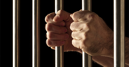 A person holding onto the bars of their jail cell.