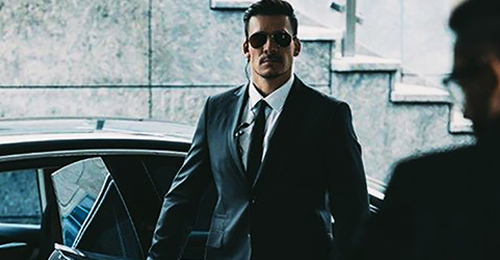 A man in suit and sunglasses standing next to a car.