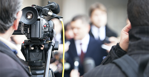 A camera is being used to record a news conference.