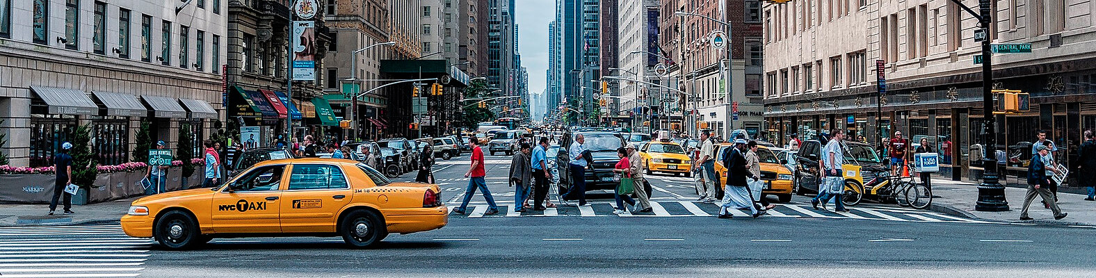 A street with people walking and a taxi passing by