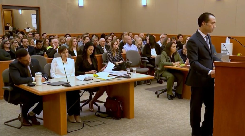 Lawyer addressing courtroom with seated audience.
